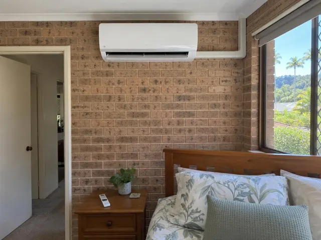 White split system on a brick bedroom wall above a wooden bedhead in Currumbin Waters