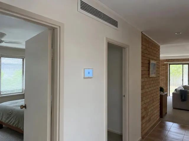 Ceiling return-air grille and wall controller in a hallway of a brick and painted home in Tugun